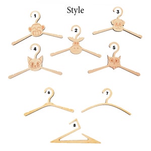 May include: A collection of eight light-colored wooden clothes hangers labeled with numbers one through eight. Five hangers feature animal head designs including a monkey, cow, dog, cat, and owl. Three hangers have plain, curved, or angular shapes.