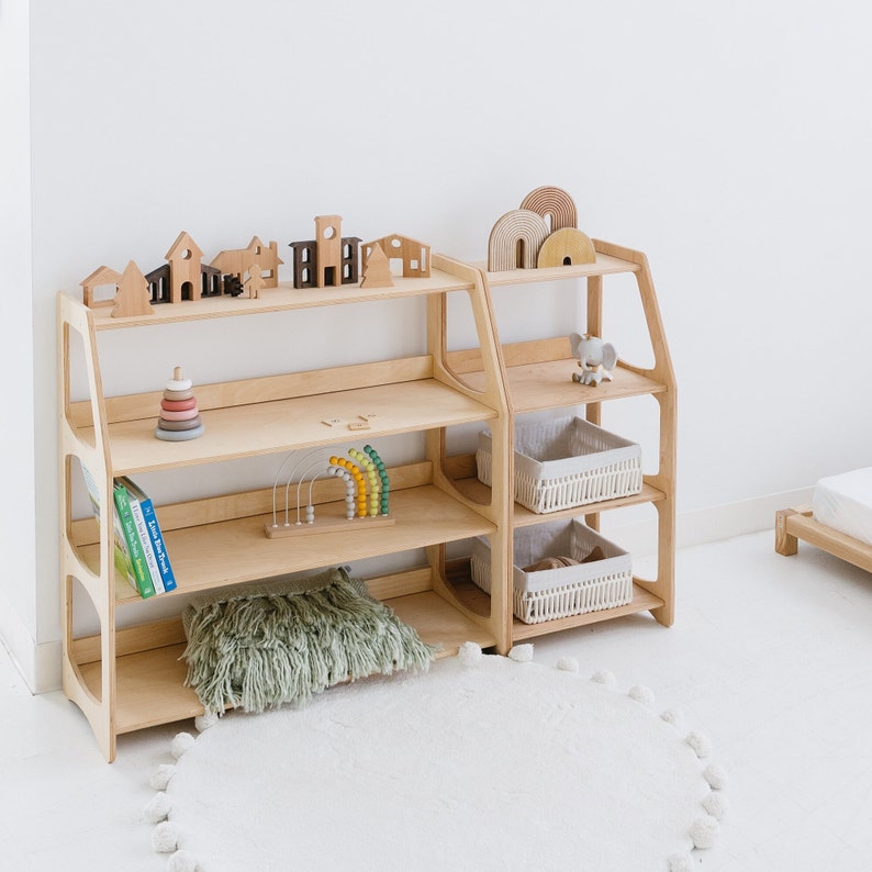 May include: Two wooden shelves with multiple shelves, one on top of the other. The shelves are filled with wooden toys, books, and baskets. The shelves are made of light wood and have a natural finish.