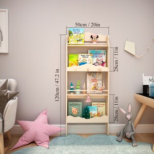 May include: A light-colored wooden bookshelf, 47.2 inches tall and 20 inches wide, with three shelves. The shelves hold children's books and decorative items. A pink star-shaped pillow and a gray stuffed rabbit are on the floor.