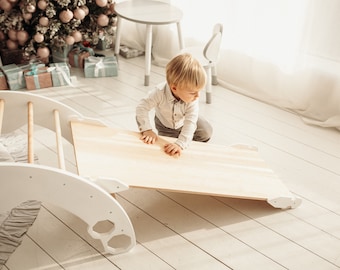 May include: A white wooden play structure with a slide and a climbing ladder. A young child is playing on the slide.