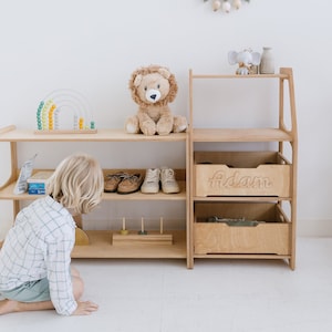 May include: A wooden shelf unit with two shelves and two drawers. The top shelf has a stuffed lion toy and a small elephant figurine. The bottom drawer is labeled "Adam".