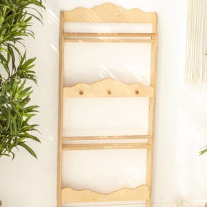 May include: A light wood wall shelf with three shelves and three hooks. The shelf has a scalloped edge and is made of unfinished wood.
