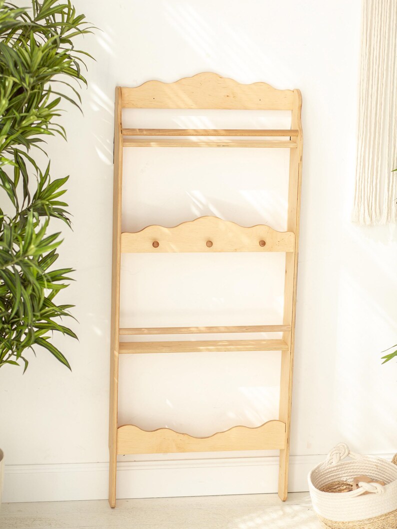 May include: A light wood wall shelf with three shelves and three hooks. The shelf has a scalloped edge and is made of unfinished wood.