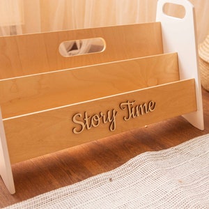 May include: A white and wood children's book organizer with three shelves. The organizer has a handle on the top and the words "Story Time" are engraved on the front.