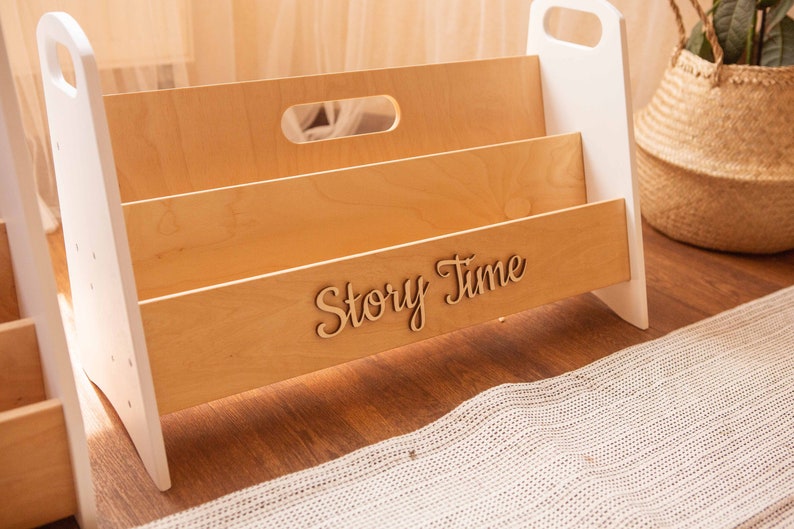 May include: A white and wood children's book organizer with three shelves. The organizer has a handle on the top and the words "Story Time" are engraved on the front.