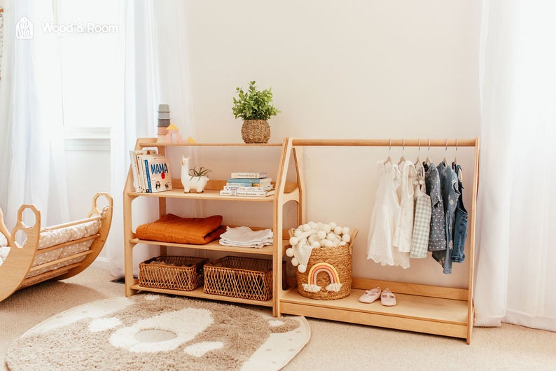 May include: Wooden children's room furniture set. Includes a three-shelf bookcase with books, blankets, and baskets, and a clothing rack with hanging clothes. A woven basket with a rainbow decor and a rug are also present.