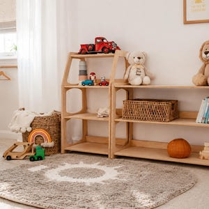 K&ouml;nnte beinhalten: Zwei helle Holzregale mit mehreren Ebenen, die verschiedene Spielzeuge enthalten, darunter ein roter Lastwagen, ein Teddyb&auml;r, ein Pl&uuml;schl&ouml;we und ein geflochtener Korb. Die Regale stehen nebeneinander und pr&auml;sentieren B&uuml;cher und kleine Holzspielzeuge.