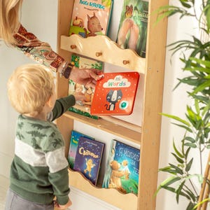 May include: A wooden bookshelf with five shelves, each holding a different book. The top shelf has a book with a fox on the cover, the second shelf has a book with a cat on the cover, the third shelf has a book with a cat on the cover, the fourth shelf has a book with a bird on the cover, and the bottom shelf has a book with a bear on the cover.