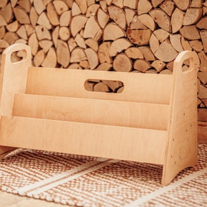May include: A light wood bookshelf with three shelves and two handles. The bookshelf is sitting on a brown and white patterned rug.