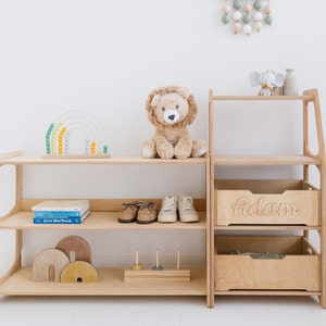 May include: A wooden shelf unit with two shelves and a drawer. The drawer is labeled "Adam". The shelf unit is filled with toys, including a stuffed lion, a rainbow abacus, and wooden blocks.