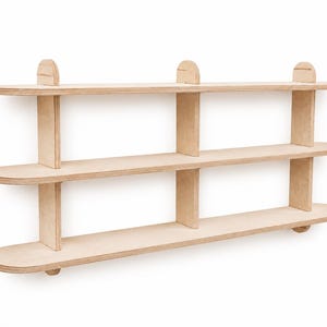 May include: A three-tiered wall-mounted shelf unit constructed from light-colored plywood. The unit features three horizontal shelves with rounded ends, supported by vertical dividers and small semi-circular accents along the top edge.