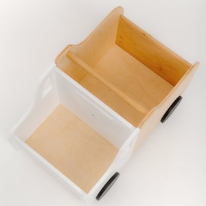 Puede incluir: Cami&oacute;n de juguete de madera blanco con dos compartimentos, uno encima del otro. El cami&oacute;n tiene ruedas negras y est&aacute; hecho de madera contrachapada.