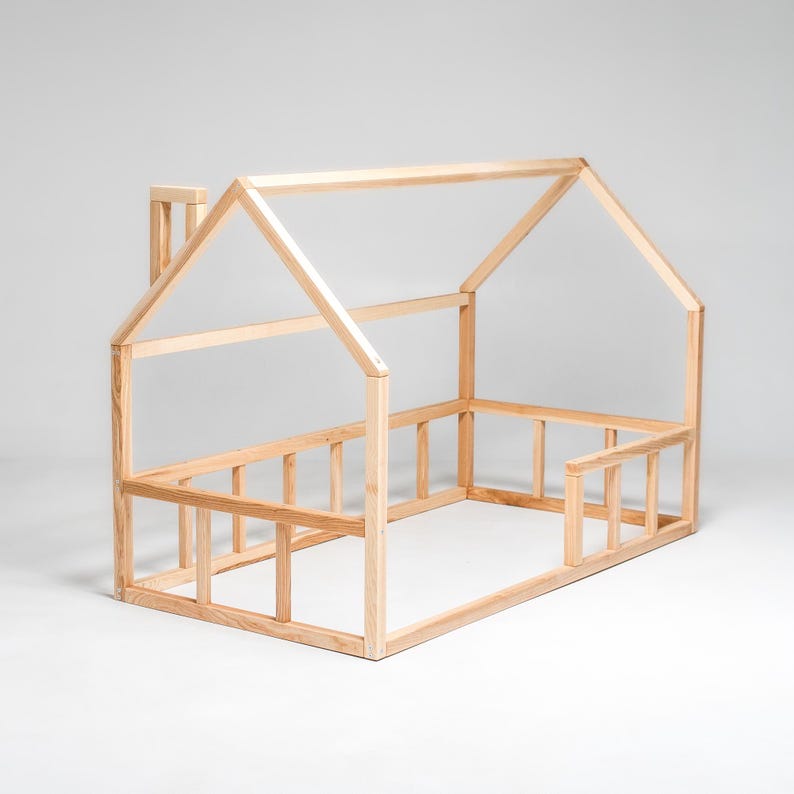 May include: A wooden house-shaped bed frame for a child. The frame is made of natural wood and has a simple design. It features a raised headboard and footboard, as well as a small chimney on the roof.