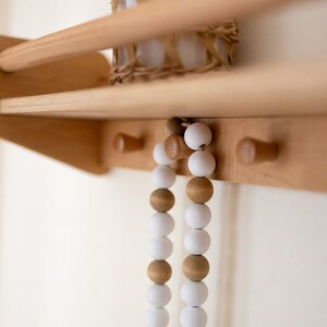 May include: Two strands of wooden beads hang from hooks on a wooden shelf. The beads are white and brown and are strung together in a repeating pattern.