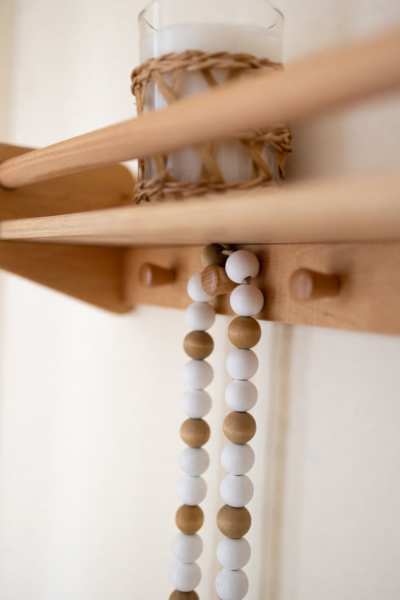 May include: Two strands of wooden beads hang from hooks on a wooden shelf. The beads are white and brown and are strung together in a repeating pattern.