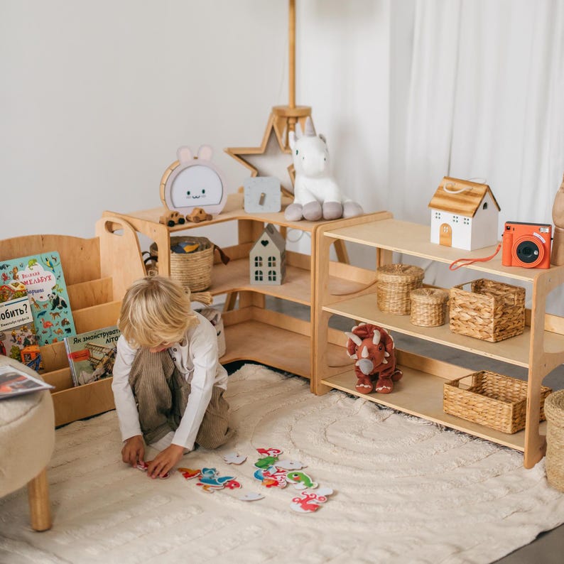 May include: A child plays with colorful animal shaped puzzle pieces on a white rug in a playroom. The room features wooden shelves with books, toys, and storage baskets. The shelves are arranged in a corner of the room.