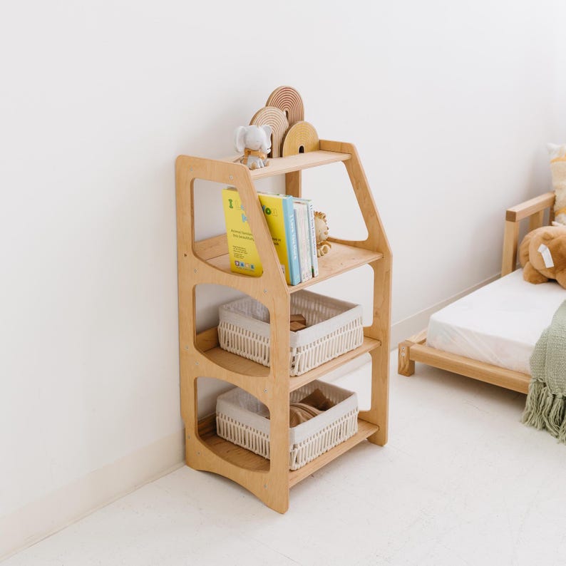 Pode incluir: Uma estante de madeira clara com tr&ecirc;s prateleiras e tr&ecirc;s cestos de vime brancos. A estante est&aacute; em um quarto com uma parede branca e uma cama de madeira.