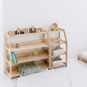 Pode incluir: Um conjunto de duas prateleiras de madeira com quatro prateleiras cada. As prateleiras s&atilde;o feitas de madeira natural e t&ecirc;m um acabamento marrom claro. As prateleiras est&atilde;o cheias de v&aacute;rios brinquedos, incluindo blocos de madeira, um brinquedo arco-&iacute;ris e uma pilha de an&eacute;is. H&aacute; um travesseiro verde felpudo na prateleira inferior.