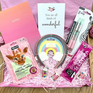 Könnte beinhalten: Geschenkbox mit rosa Seidenpapier und verschiedenen Artikeln. Enthält ein Notizbuch mit der Aufschrift "NOTES", eine Gesichtsmaske, Stifte, Haarschmuck und Süßigkeiten. Die Karte lautet: "You are all kinds of wonderful".