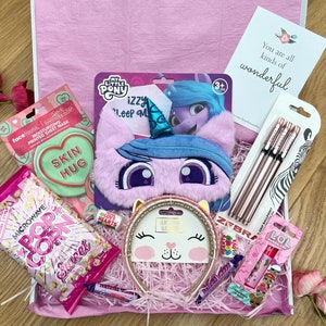 Könnte beinhalten: Eine rosa Geschenkbox gefüllt mit verschiedenen Artikeln, darunter eine My Little Pony Schlafmaske, ein rosa Stirnband mit Katzenmotiv, eine rosa herzförmige Gesichtsmaske, eine Tüte Mikrowellenpopcorn, rosa und weiße Zuckerherzen und ein Set roségoldener Stifte. Die Box enthält auch eine Karte mit dem Text "You are all kinds of wonderful."