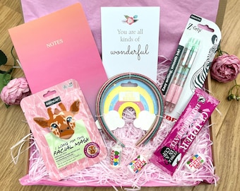 Pode incluir: Uma caixa de presente rosa com papel de seda e vários itens. Inclui um caderno com a palavra "NOTES", uma máscara facial, canetas, acessórios de cabelo e doces. O cartão diz "You are all kinds of wonderful".
