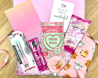Pode incluir: Uma caixa de presente rosa cheia de vários itens, incluindo um caderno rosa com a palavra "NOTES" na capa, duas canetas rosa com glitter, uma máscara facial rosa, um saco rosa de pipoca para microondas e um par de meias rosa com estampa de gato. A caixa está cheia de papel picado rosa e branco. Também está incluído um cartão com o texto "You are all kinds of wonderful".