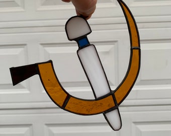 Könnte beinhalten: Ein hängender Fensterschmuck aus Buntglas, der einen Hammer und eine Sichel in Gelb und Weiß mit einem blauen Akzent darstellt.