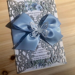 Puede incluir: Una invitaci&oacute;n de corte l&aacute;ser con brillo plateado, un lazo de sat&eacute;n azul claro y una mariposa de brillo plateado. El texto de la invitaci&oacute;n dice: "mor haberme permitido llea i vida. Llena de in en m pad nd esia lvd. ida: 5:00PM-7:00 Baile: 7:00PM-12:00AM Paul Armenian Cha 57 N First St. Fresno CA, 93"