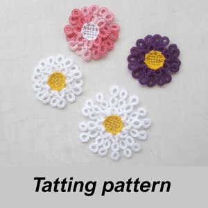 Puede incluir: Cuatro flores de ganchillo en blanco, rosa y morado con centros amarillos. Las flores están dispuestas sobre un fondo de tela blanca. El texto "Tatting pattern" está escrito debajo de las flores.