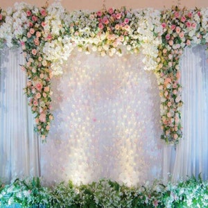以下が含まれることがあります： 白、ピンク、ピーチ色の花が咲き誇る花の背景。 花はアーチ状に配置され、白いカーテンの両側に滝のように花が咲き乱れています。 緑の葉がベースを飾り、ロマンチックな雰囲気を作り出しています。