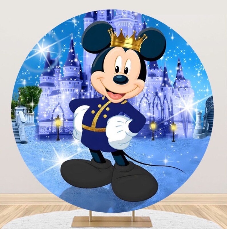 K&ouml;nnte beinhalten: Ein runder Hintergrund mit Mickey Mouse in einem k&ouml;nigsblauen Outfit mit goldenen Verzierungen und einer goldenen Krone. Der Hintergrund zeigt ein Schloss unter einem Sternenhimmel, mit einem hellblauen und wei&szlig;en Farbschema. Der Hintergrund wird von einem goldenen St&auml;nder getragen.
