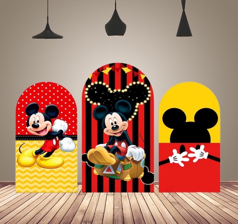 May include: Three Mickey Mouse themed cardboard cutouts for a party. The cutouts are shaped like arches and feature Mickey Mouse in different poses. The first cutout features Mickey Mouse in a red and yellow outfit with a yellow and white polka dot background. The second cutout features Mickey Mouse in a red and yellow outfit with a black and red striped background. The third cutout features Mickey Mouse's head and hands in a red and yellow outfit with a yellow background.