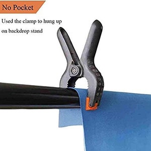 Puede incluir: Una abrazadera negra con detalles naranjas se utiliza para sujetar un tel&oacute;n de fondo azul a una barra de metal negra. El texto "No Pocket" y "Used the clamp to hung up on backdrop stand" es visible en la imagen.