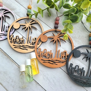 Könnte beinhalten: Vier Holzornamente mit einer Palme und dem Text "Beach Life" in einem Ausschnittdesign. Die Ornamente sind in verschiedenen Farben: rosa, braun, naturholz und schwarz. Drei kleine Glasflaschen mit ätherischen Ölen sind ebenfalls im Bild.