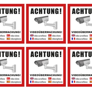 Könnte beinhalten: Sechs rote Schilder mit weißen Rändern und schwarzem Text, der "ACHTUNG! VIDEOÜBERWACHUNG!" lautet. Jedes Schild zeigt eine schwarz-weiße Überwachungskamera mit einem grauen Arm. Die Schilder enthalten auch die Wörter "video surveillance", "vidéosurveillance", "video izleme" und "videovigilancia" in Englisch, Französisch, Türkisch und Spanisch.