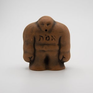 May include: A brown ceramic figurine of a person with the Hebrew word "אומץ" (meaning "courage") inscribed on the chest. The figurine has a hole in the top of its head, suggesting it may be a whistle or incense burner.