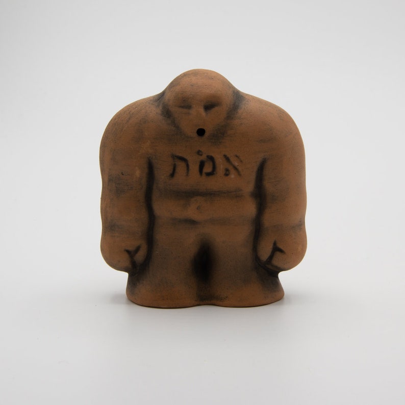 May include: A brown ceramic figurine of a person with the Hebrew word "אומץ" (meaning "courage") inscribed on the chest. The figurine has a hole in the top of its head, suggesting it may be a whistle or incense burner.