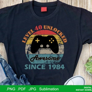May include: A black t-shirt with a vintage-style graphic design. The graphic features a retro-style video game controller with the text "Level 40 Unlocked Awesome Since 1984".