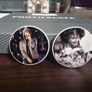 May include: Two round white photo slates with black and white images. One slate features a man wearing a hooded sweatshirt and holding a microphone. The other slate features a young person with long hair holding a baby.