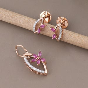 May include: Rose gold jewelry set featuring a pendant and matching earrings. The pendant and earrings have a leaf-like design with pink gemstone flower accents and white gemstone detailing.