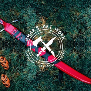 May include: A red and black sword with a leather scabbard. The scabbard has a black and white logo with the text "UMAR'S ART WORK CREATE INNOVATE MOTIVATE".