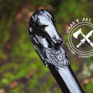 May include: Black wooden walking stick with a carved dog head handle. The handle is detailed with fur and the dog's head is looking to the side. The stick is polished and has a smooth finish. The image also includes a logo with the text "UMAR'S ART WORK" and the words "CREATE, INNOVATE, MOTIVATE".