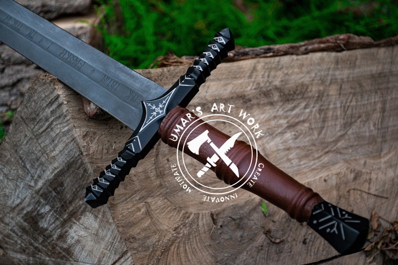 May include: A detailed image of a black and silver sword with a brown handle, resting on a wooden surface. The sword features intricate designs and inscriptions on the blade. The handle has a leather-like appearance. The image includes a logo that says "UMAR'S ART WORK".