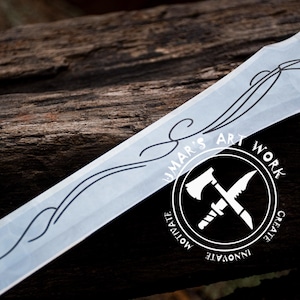 May include: A close-up of a silver sword with a decorative design and a horse etched into the blade. The sword is resting on a wooden surface. The image also includes a logo with the text "UMAR'S ART WORK" and the words "CREATE, INNOVATE, MOTIVATE" around the logo.
