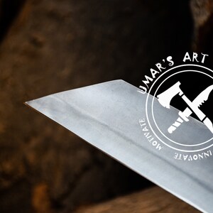K&ouml;nnte beinhalten: Nahaufnahme einer scharfen, silbernen Klinge mit einem runden Logo, auf dem "UMAR'S ART WORK" steht, umgeben von den W&ouml;rtern "MOTIVATE", "INNOVATE" und "CREATE". Das Logo zeigt eine gekreuzte Axt und ein Messer.