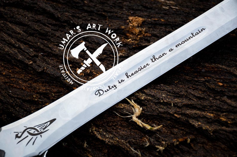 May include: A silver knife with a black handle and a white inscription that reads "Duty is heavier than a mountain". The knife is on a brown wooden surface. The inscription is in a cursive font. The knife has a black and white logo on the handle that reads "Jumar's Art Work".