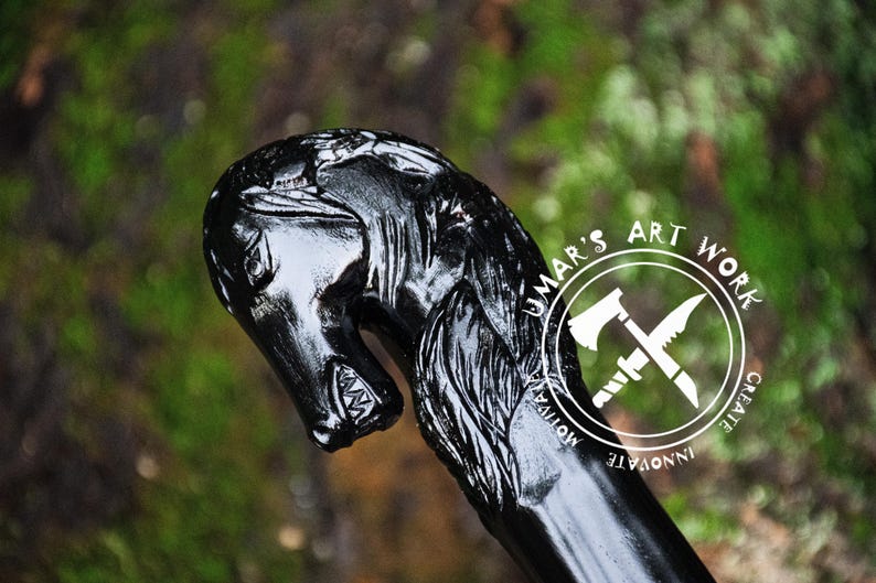 May include: A black wooden walking stick with a carved horse head handle. The horse head is detailed with a mane and a mouth with teeth. The stick is polished and has a smooth finish. The text "UMAR'S ART WORK CREATE INNOVATE MOTIVATE" is printed on the stick.