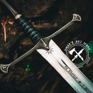 May include: A detailed image of a silver sword with a black leather-wrapped handle. The blade has etched inscriptions and a star design. The hilt features gold accents. The sword is set against a dark, textured background, with the text "UMAR'S ART WORK" in a circular logo.