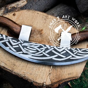 May include: A crescent-shaped blade with a dark, etched Celtic knot pattern on the metal surface. The tool features two wooden handles attached to the top of the blade. A circular logo with the text UMAR'S ART WORK is visible on the blade.