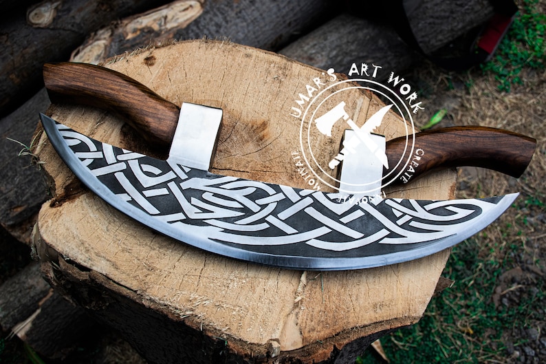 May include: A crescent-shaped blade with a dark, etched Celtic knot pattern on the metal surface. The tool features two wooden handles attached to the top of the blade. A circular logo with the text UMAR'S ART WORK is visible on the blade.